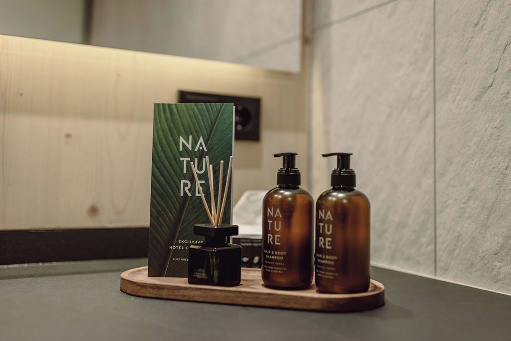 Uma bancada de banheiro com apresentação de produtos com tema natural, incluindo um difusor, uma garrafa de shampoo e uma garrafa de condicionador.