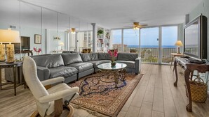A modern living room with a grey sectional sofa, a round coffee table, and a large window offering a view of the sea. - Shoreline Towers 3063 (Destin)