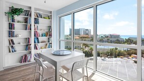 A modern room with a large window, white walls, and a bookshelf filled with books. - Shoreline Towers 3063 (Destin)