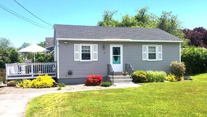 A single-story house with a front porch, a small garden with red flowers, and a clear blue sky.