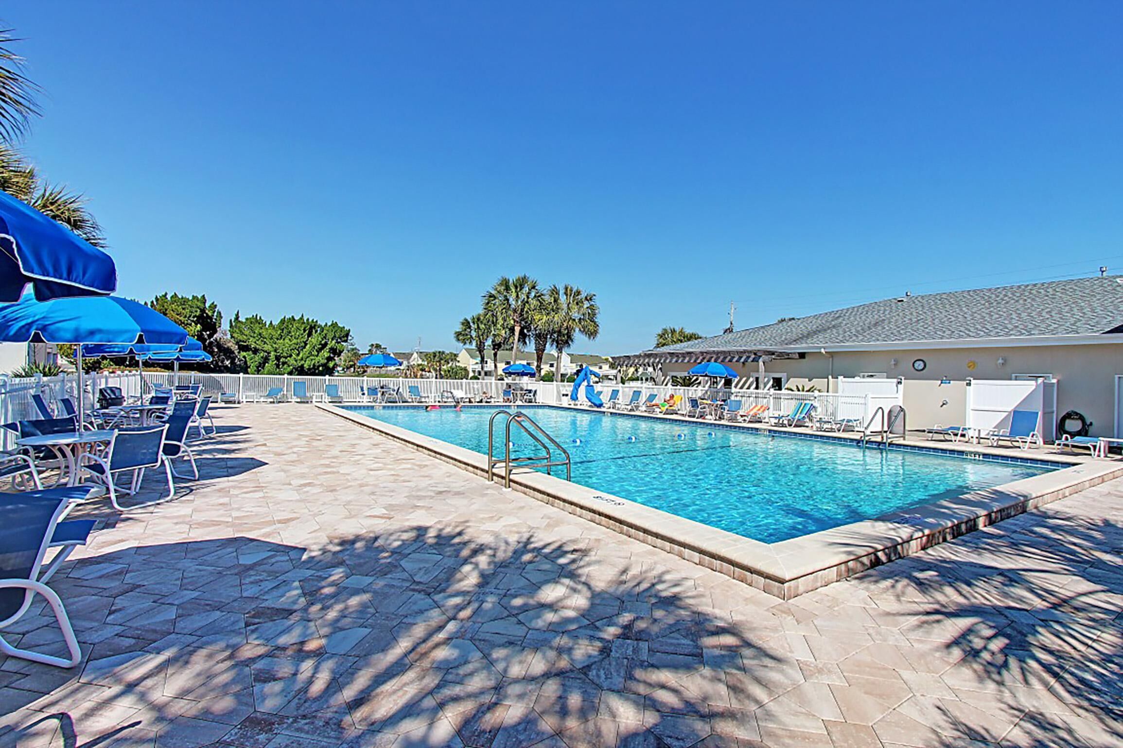 A rectangular swimming pool with a tiled deck, surrounded by lounge chairs and umbrellas.