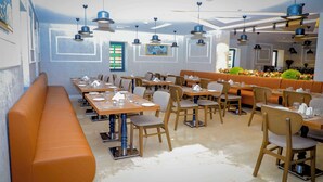 A modern restaurant with wooden tables and chairs, a long orange bench, and pendant lighting. - Best Western Premier Dj Hotel (Djibouti)