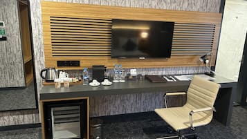 A modern hotel room with a flat-screen TV, a coffee station, a desk with a laptop, and a leather chair.
