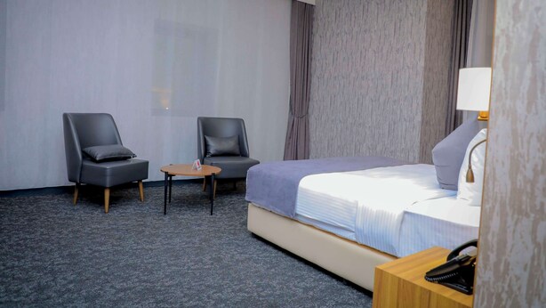 A hotel room with a bed, two chairs, a small table, and a nightstand with a lamp. - Best Western Premier Dj Hotel (Djibouti)
