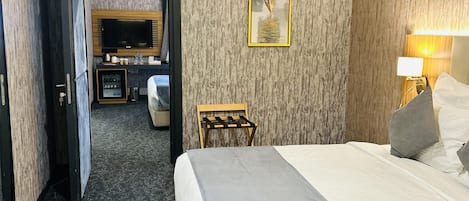 A hotel room with a bed, a desk, a television, and a painting on the wall.