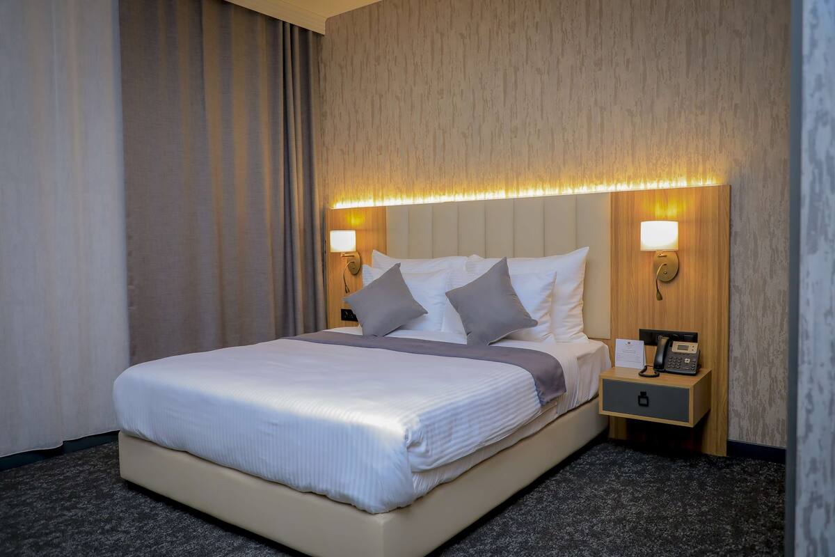 Una habitación de hotel con una cama grande, dos mesitas de noche y una lámpara de pared.
