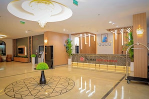 Ein Hotel-Empfangsbereich mit modernem Design, der ein Empfangspult, eine Chandelier und eine digitale Informationsstation beinhaltet.