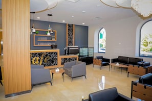 A modern lounge area with seating, a coffee station, and a large window providing natural light.