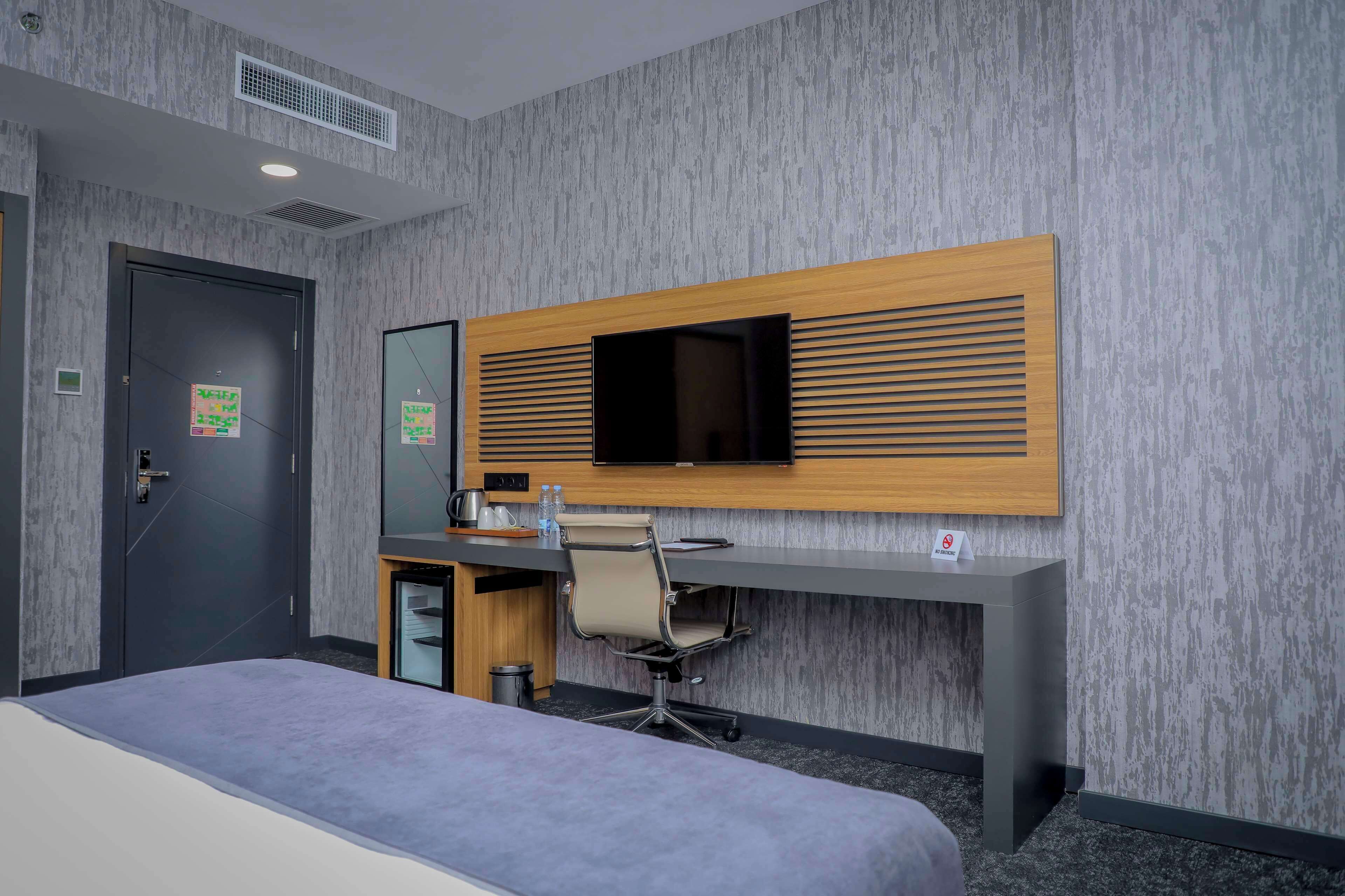A hotel room with a bed, a desk with a chair, a television, and a door.