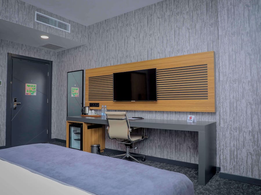 Una habitación de hotel con cama, escritorio, silla, televisión y puerta.