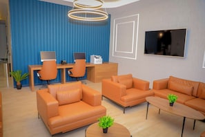 A modern office space with leather sofas, a wooden desk, and a flat-screen TV.