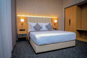 Una habitación de hotel con una cama grande, dos mesitas de noche, un armario y lámparas de pared.