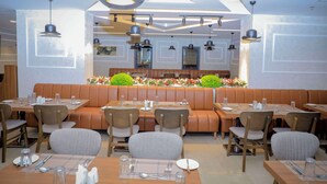 Un restaurante con cabinas y mesas, iluminación colgante moderna y una decoración floral central.