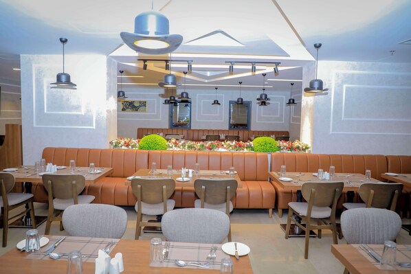 Un restaurante con cabinas y mesas, iluminación colgante moderna y una decoración floral central.