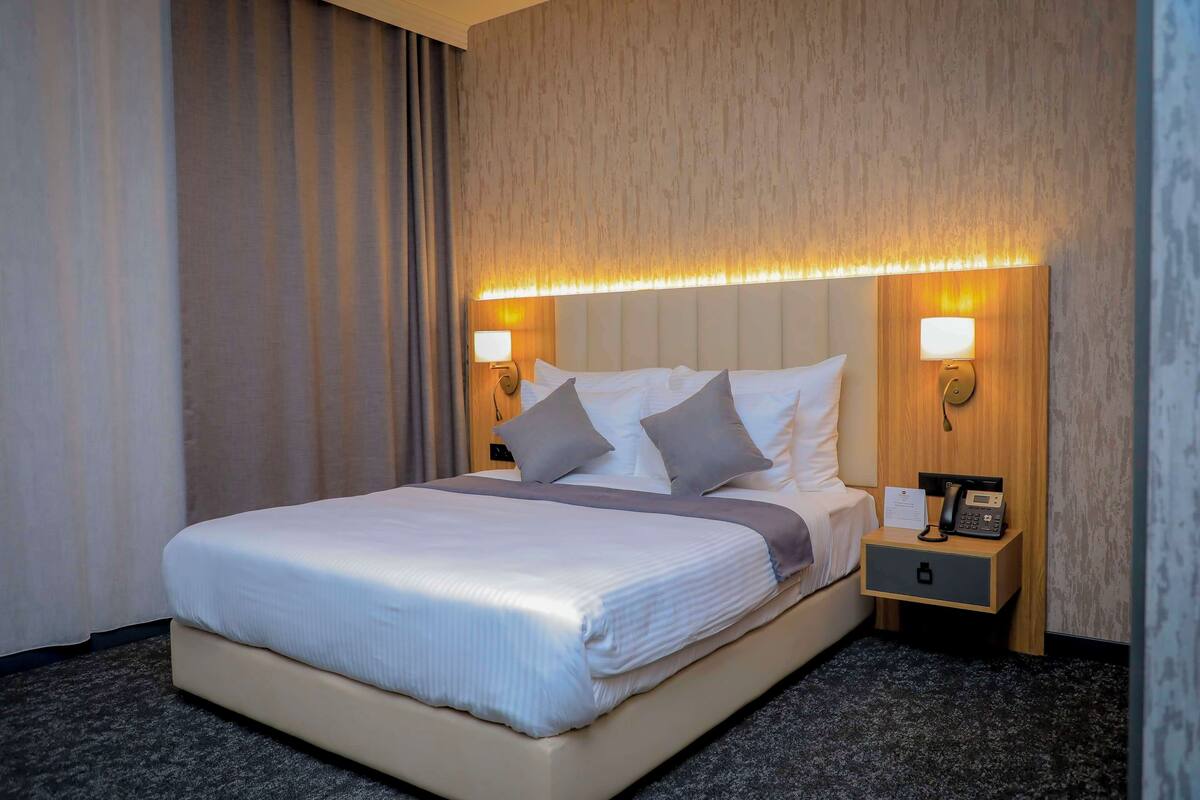 Ein Hotelzimmer mit einem großen Bett, zwei Nachttischen, einer Wandlampe und einem Nachtkästchen.