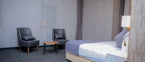 A hotel room with a bed, two chairs, a small table, a lamp, and a telephone on a wooden side table.