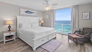 A bedroom with a large bed, a ceiling fan, a view of the ocean, and a wicker chair. - Shoreline Towers 1114 (Destin)