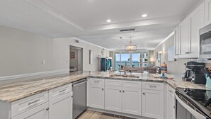 A modern kitchen with white cabinetry, a granite countertop, and a large island. - Shoreline Towers 1114 (Destin)