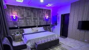 Une chambre moderne avec un grand lit, un canapé, une petite table et un téléviseur fixé au mur.