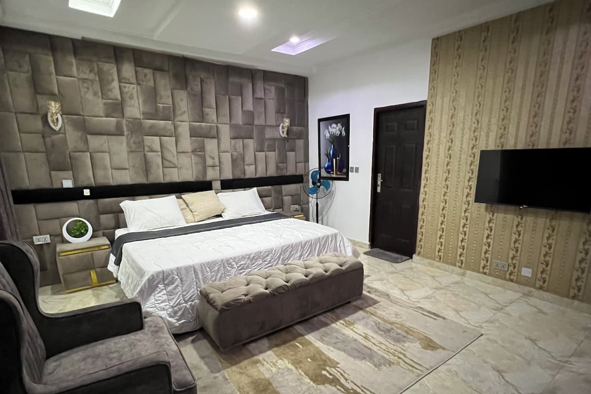 A modern bedroom with a large bed, a sofa, a TV, and a patterned wall.