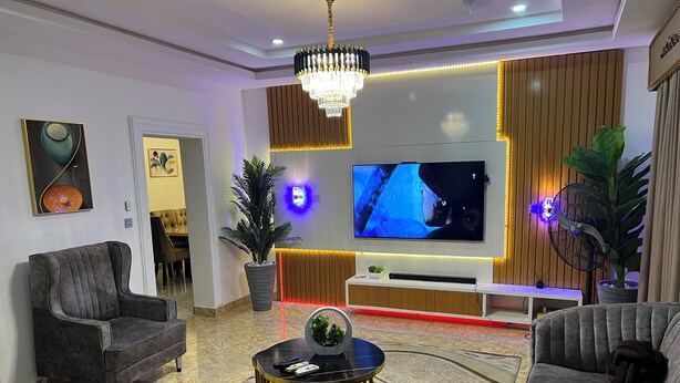 Un salon moderne doté d’un grand téléviseur à écran plat, de sièges confortables, d’un lustre et de plantes décoratives.