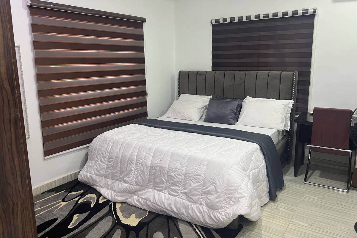 A bedroom with a bed, a chair, and a window with blinds.