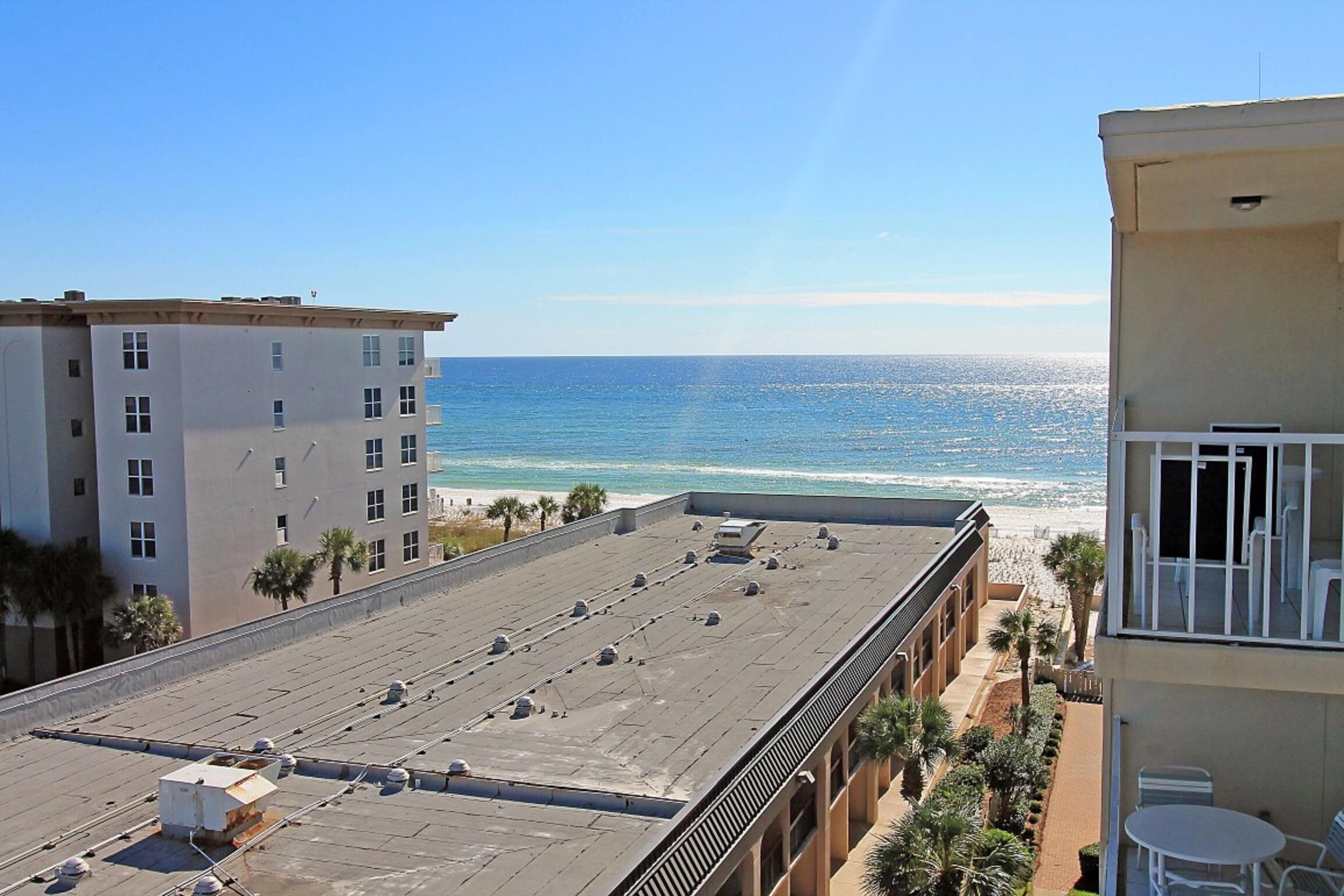 A rooftop with a view of the beach, buildings, and palm trees.