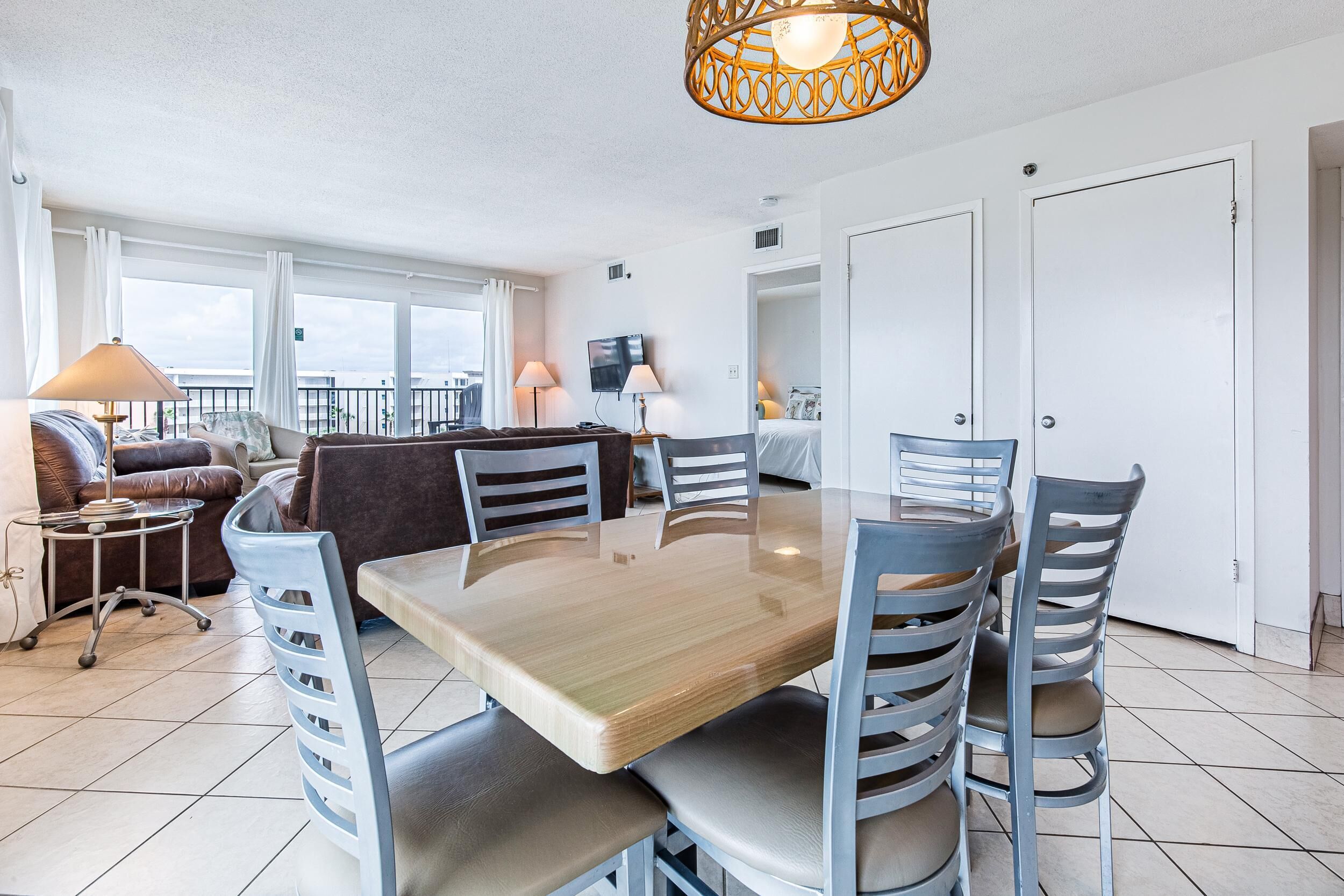A modern living room with a wooden dining table, grey chairs, a sofa, and a balcony with a view.