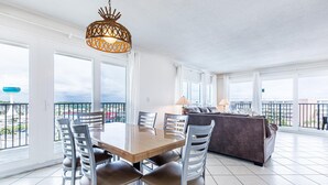 A spacious living area with a wooden dining table, multiple chairs, a sofa, and a balcony with a view. - Sea Oats 712 (Fort Walton Beach)
