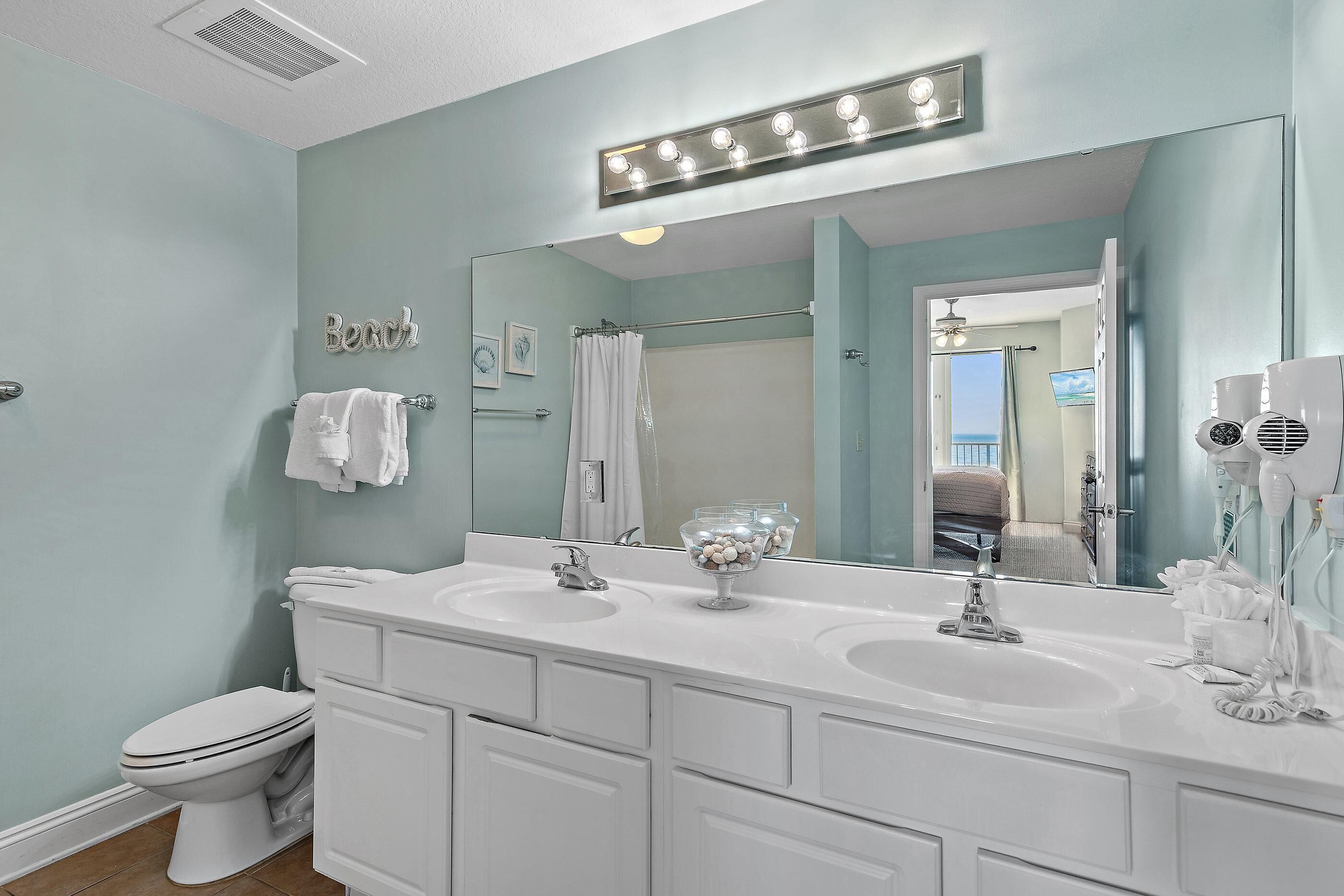 A bathroom with a double sink, a toilet, a large mirror, and a vanity with drawers.