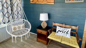 Una habitación con pared azul, un banco de madera con cojín, una silla colgante, una mesita con lámpara y un cartel que dice 'HOME'.