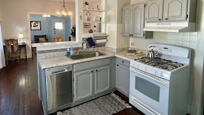 Una cocina con armarios blancos, lavavajillas integrado, estufa a gas y salpicadero de azulejos.