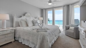 Ein Schlafzimmer mit einem großen Bett, einem Deckenventilator, einem Nachttisch, einer Kommode und Blick auf den Ozean.