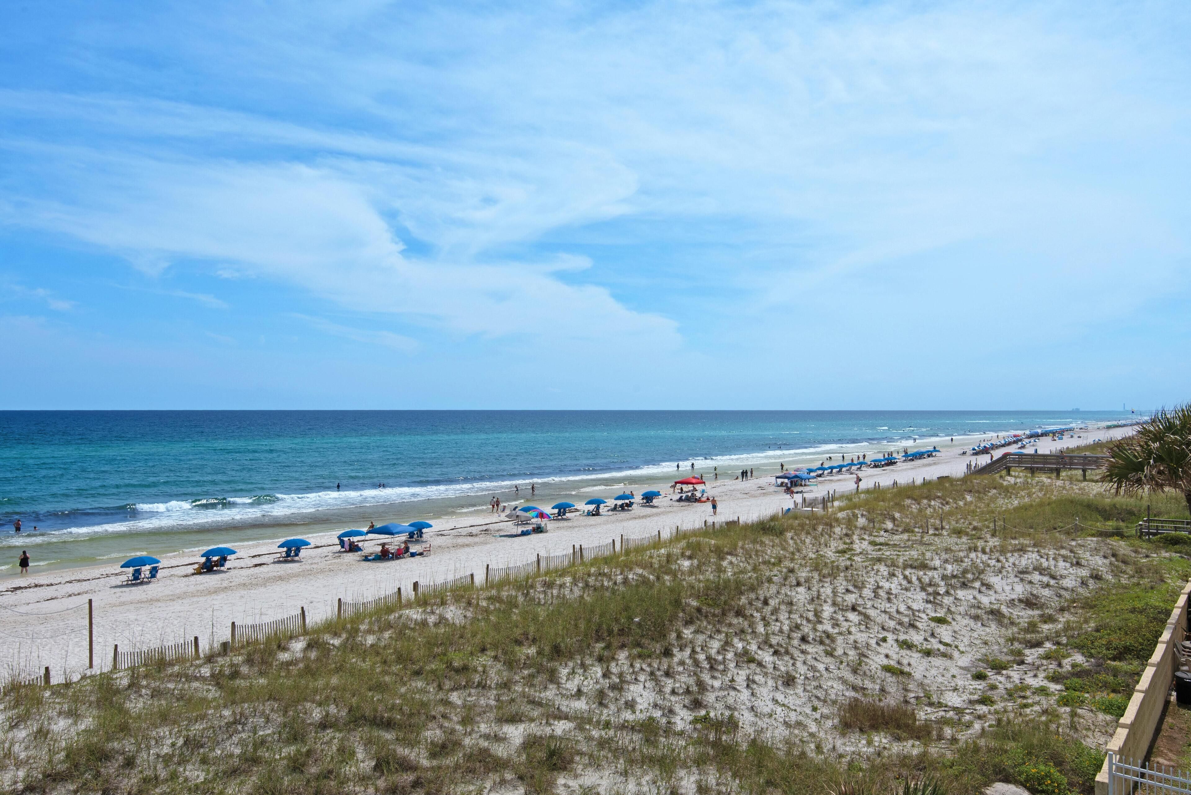 Une plage avec un rivage sablonneux, une clôture en bois et plusieurs parasols bleus.