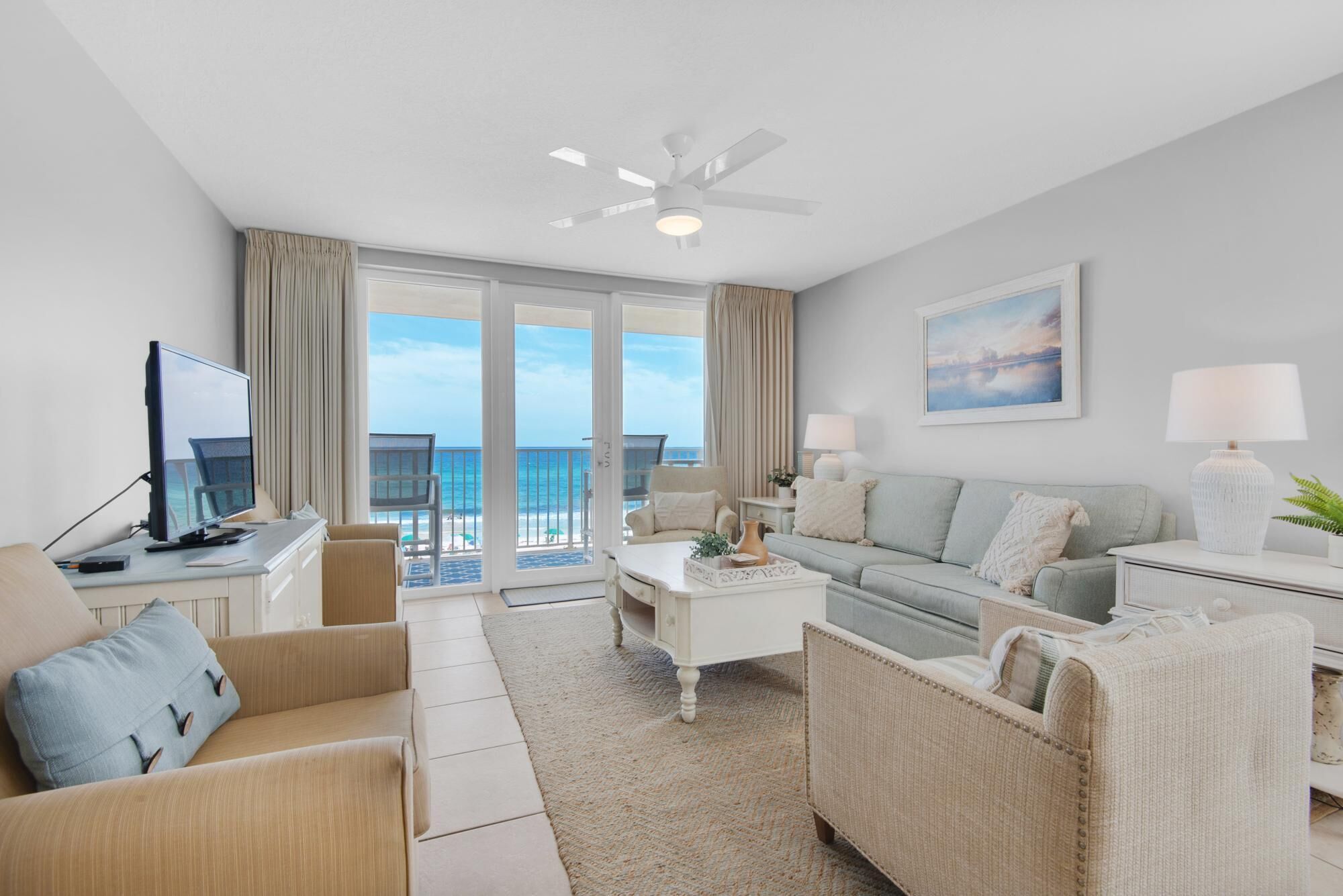 A modern hotel room with a balcony, a flat-screen TV, a sofa, a coffee table, and a lamp.