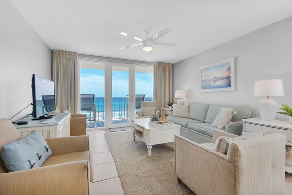 A modern hotel room with a balcony, a flat-screen TV, a sofa, a coffee table, and a lamp.