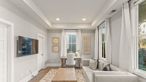 A modern living room with a sofa, a coffee table, and a desk with a chair. There is a large window with curtains, a TV mounted on the wall, and a patterned rug on the floor. - Grange Getaway at Serenbe (Palmetto)