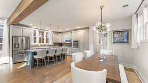 A modern kitchen with white cabinetry, stainless steel appliances, and a wooden dining table with white chairs. - Grange Getaway at Serenbe (Palmetto)