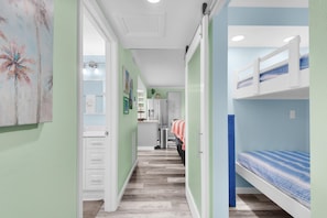 A narrow hallway with a bunk bed on the right, a kitchenette in the background, and a door leading to another room.