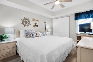 A bedroom with a large bed, a ceiling fan, a TV, and a wardrobe.