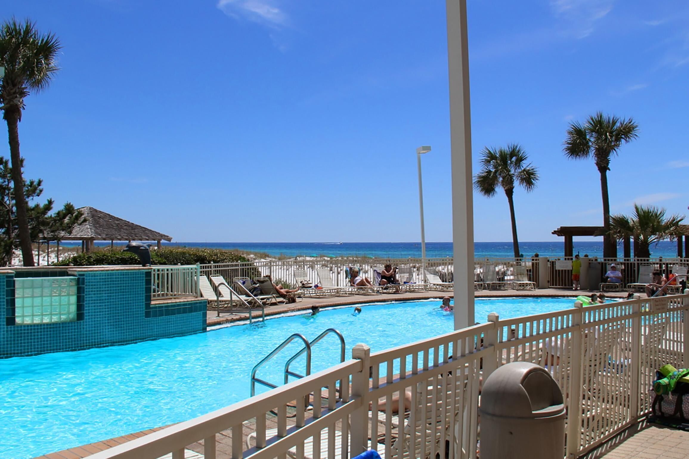 Un espace piscine avec vue sur la plage, des chaises longues et des palmiers.