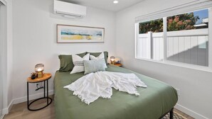 A bedroom with a green bedspread, a framed painting above the bed, and a window with a view of greenery. - Cozy 1bd 1ba Sleeps 3 Close to Disney (Garden Grove)
