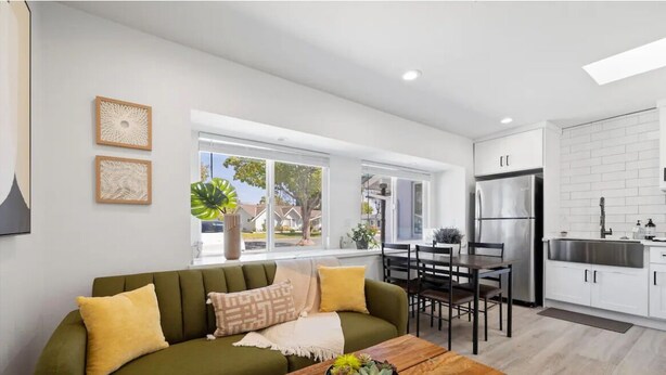 A modern living room with a green sofa, wooden coffee table, and a dining area with a table and chairs. - Cozy 1bd 1ba Sleeps 3 Close to Disney (Garden Grove)