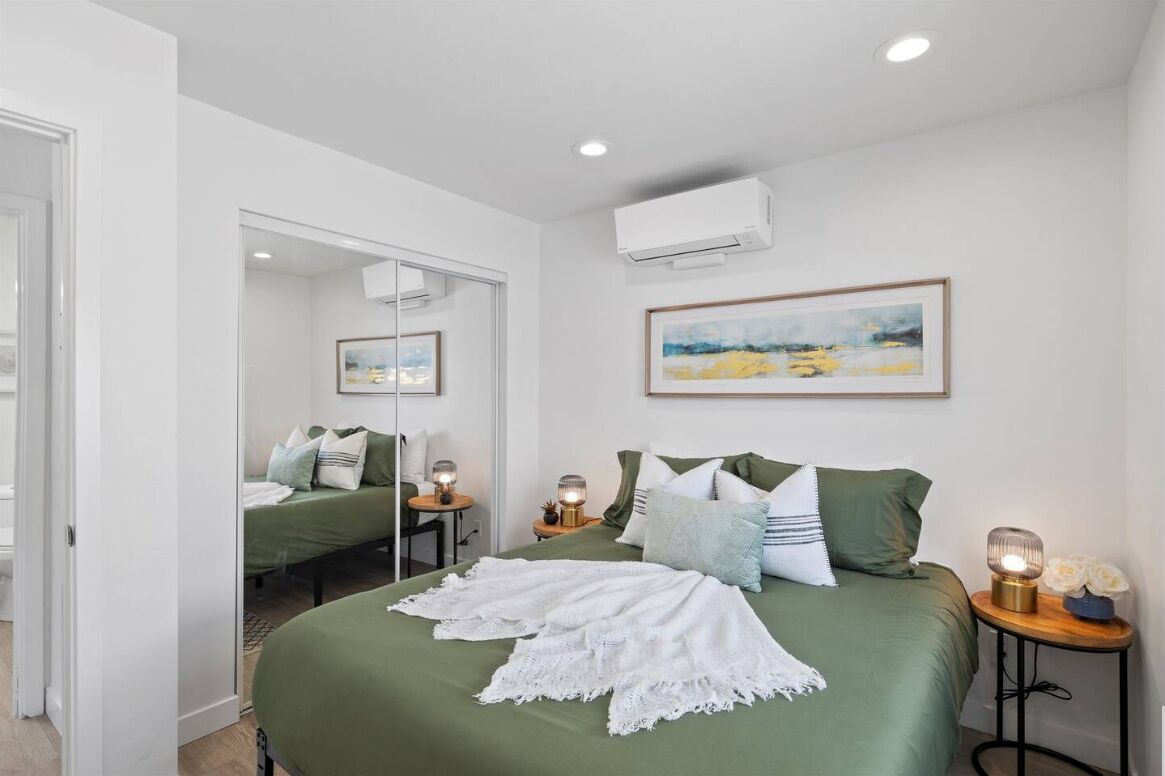 A bedroom with a green bed, white bedding, a painting, and a bedside table with a lamp.