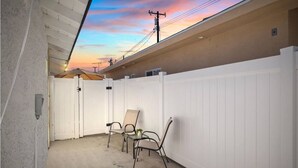 A covered patio area with a white fence, concrete floor, and metal chairs. - Cozy 1bd 1ba Sleeps 3 Close to Disney (Garden Grove)