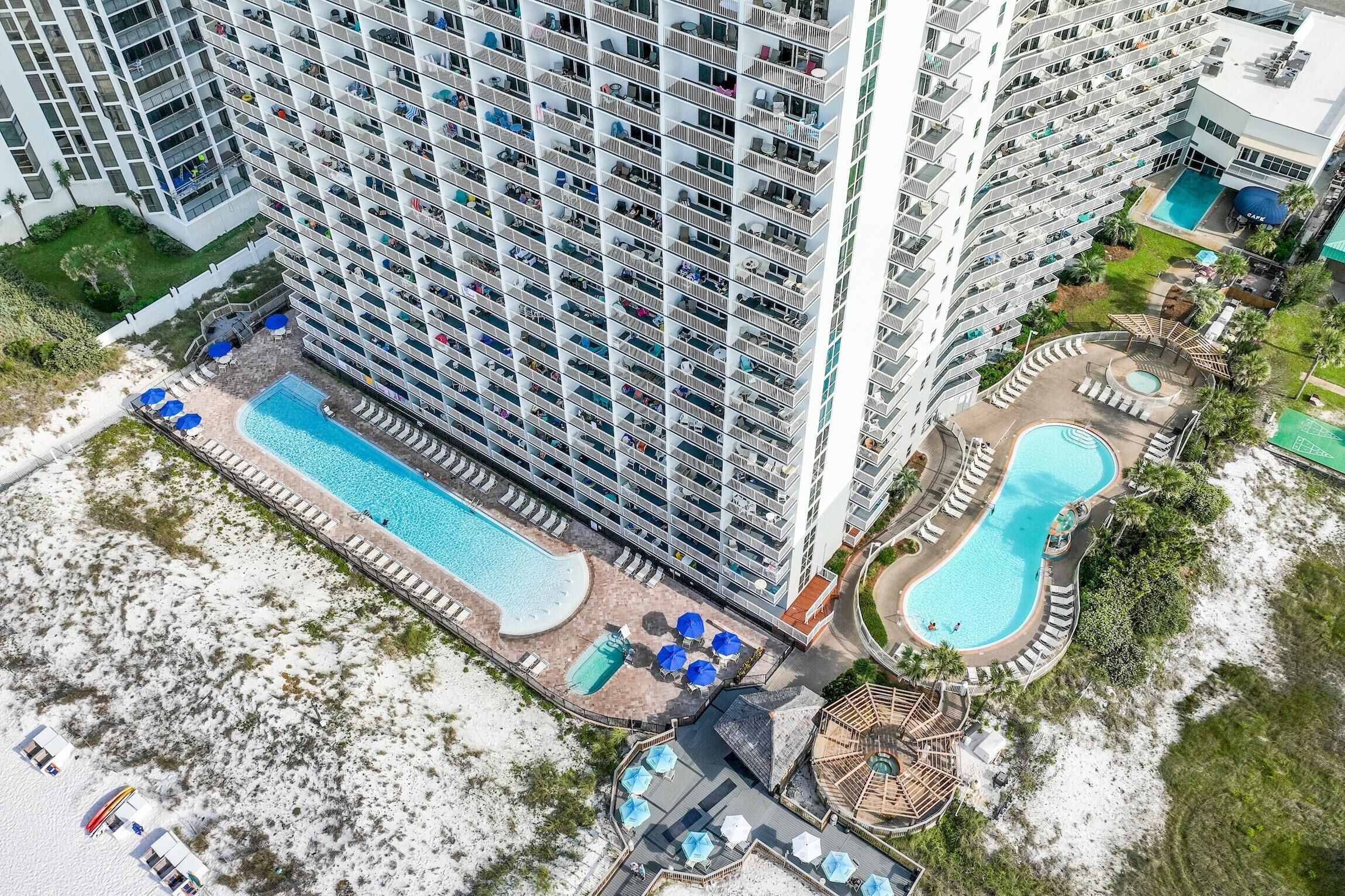 Un hôtel de grande hauteur doté de nombreux balcons, d’un grand espace piscine avec des chaises longues et d’une piscine plus petite séparée.
