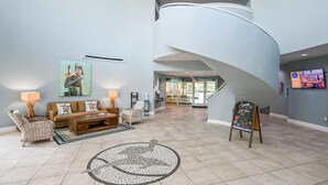 Un hall d’entrée spacieux avec un escalier en courbe, un coin salon comprenant un canapé et des fauteuils, une table basse et un motif de mosaïque ornant le sol.