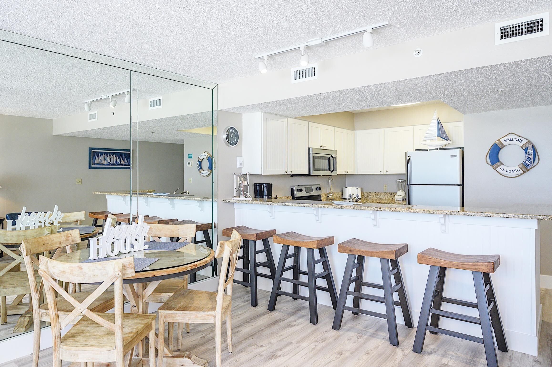 A modern kitchen with white cabinets, a central island with stools, a microwave, and a refrigerator.
