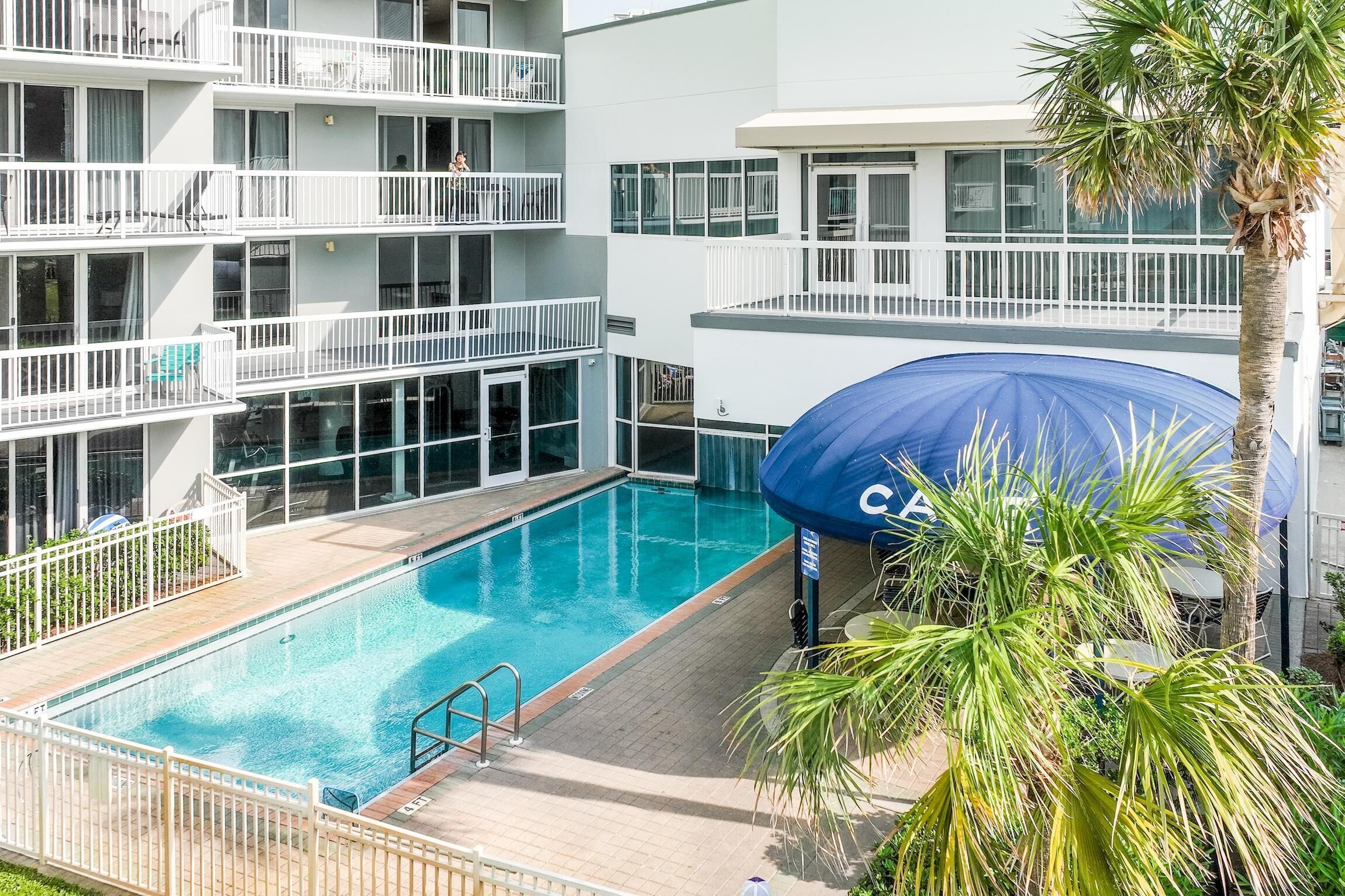 Un hôtel doté d’une piscine, de plusieurs balcons et d’un palmier.
