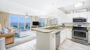 A modern kitchen with a central island, stainless steel appliances, and a large window overlooking the ocean.